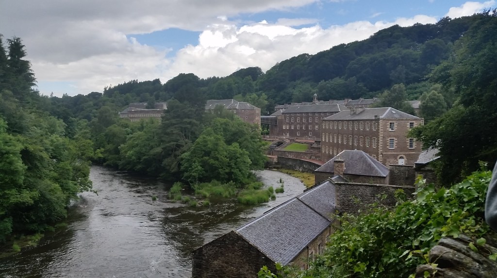 Many four-story buff brick buildings along a river in a narrow valley