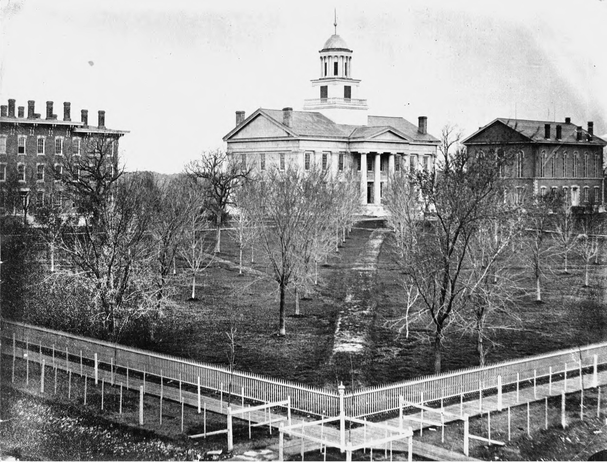 The State University Campus around 1869 showing three buildings and a decorative fence.